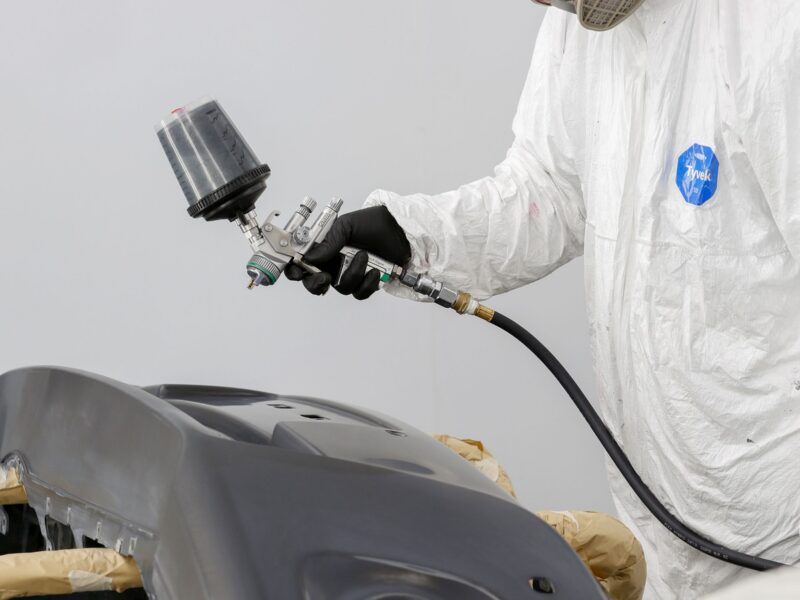 Technician in protective suit spray-painting a body panel